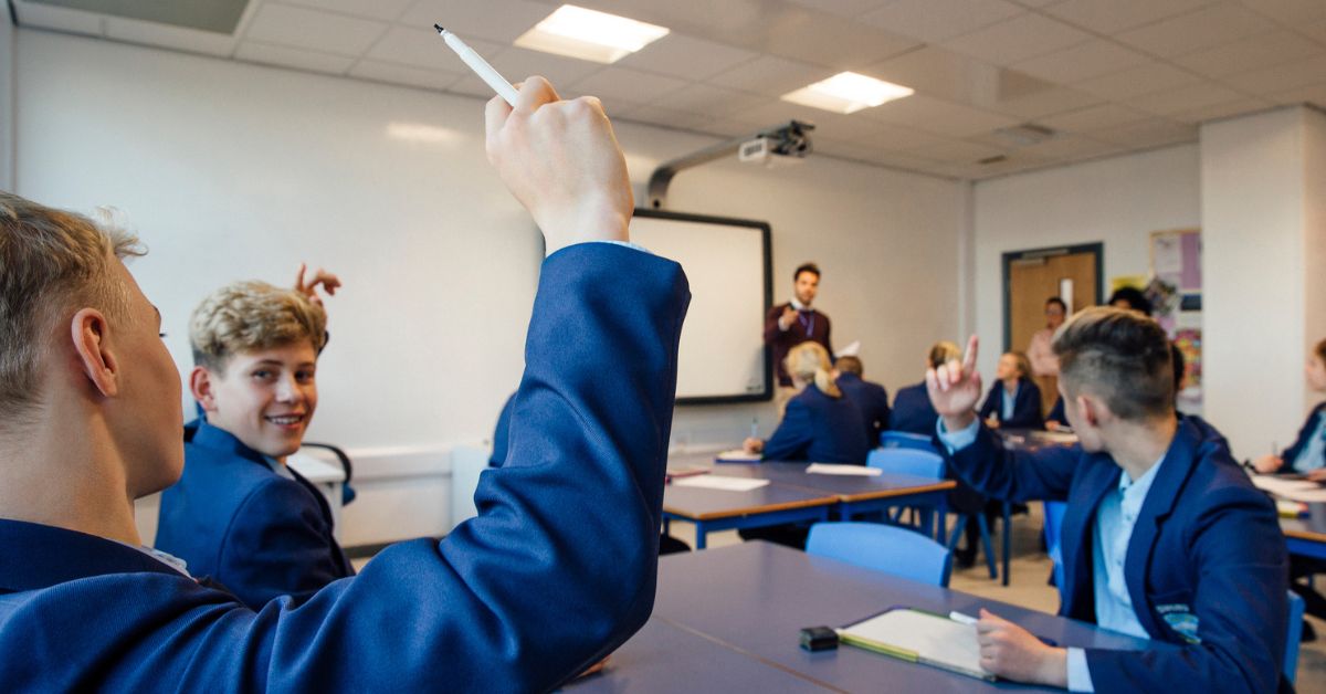 Classroom of students with one raising hand asking question