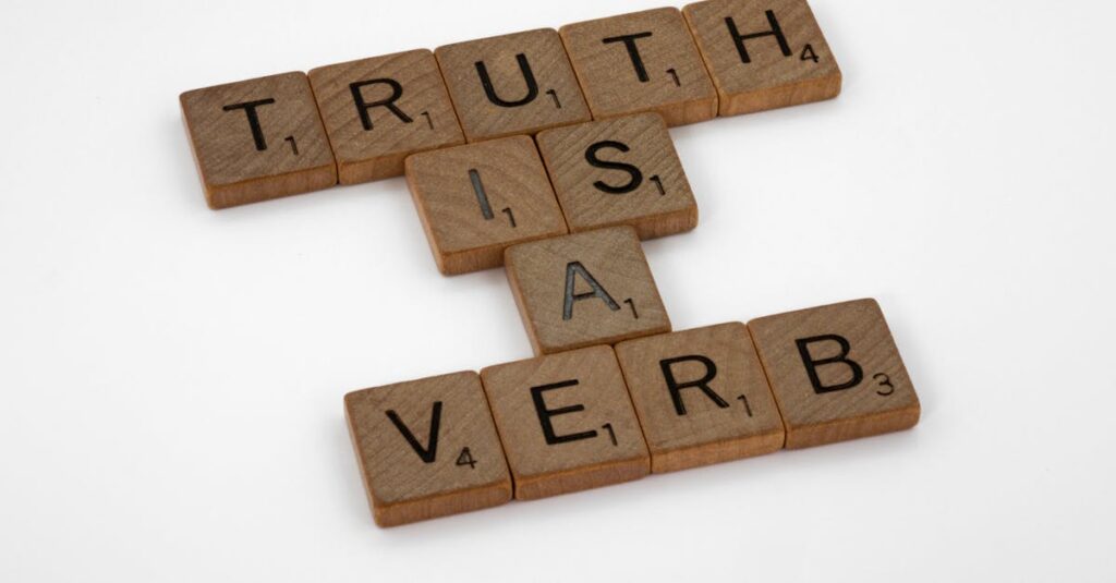 Scrabble tiles arranged on a white background spelling 'Truth is a Verb' for creative representation.