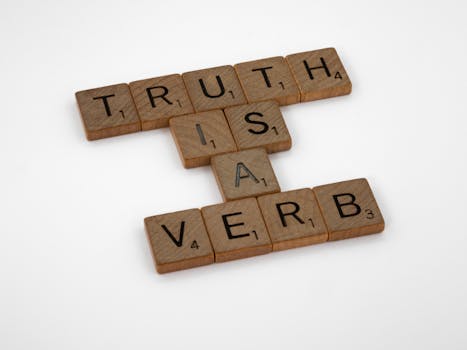 Scrabble tiles arranged on a white background spelling 'Truth is a Verb' for creative representation.